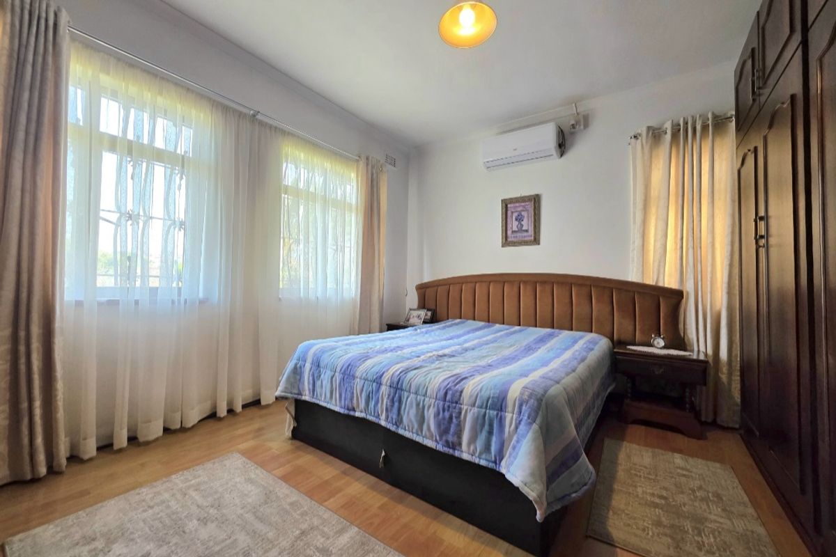 A well-maintained bedroom featuring laminate flooring, a built-in wardrobe, and a wall-mounted split-system air conditioner for climate control.