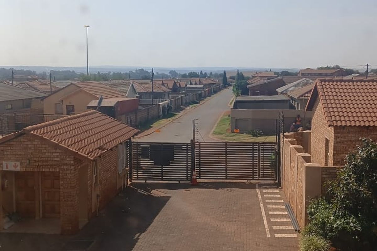 Elevated view of the townhouse complex entrance, featuring a paved driveway, secure gated access, and brick-built garage structure.