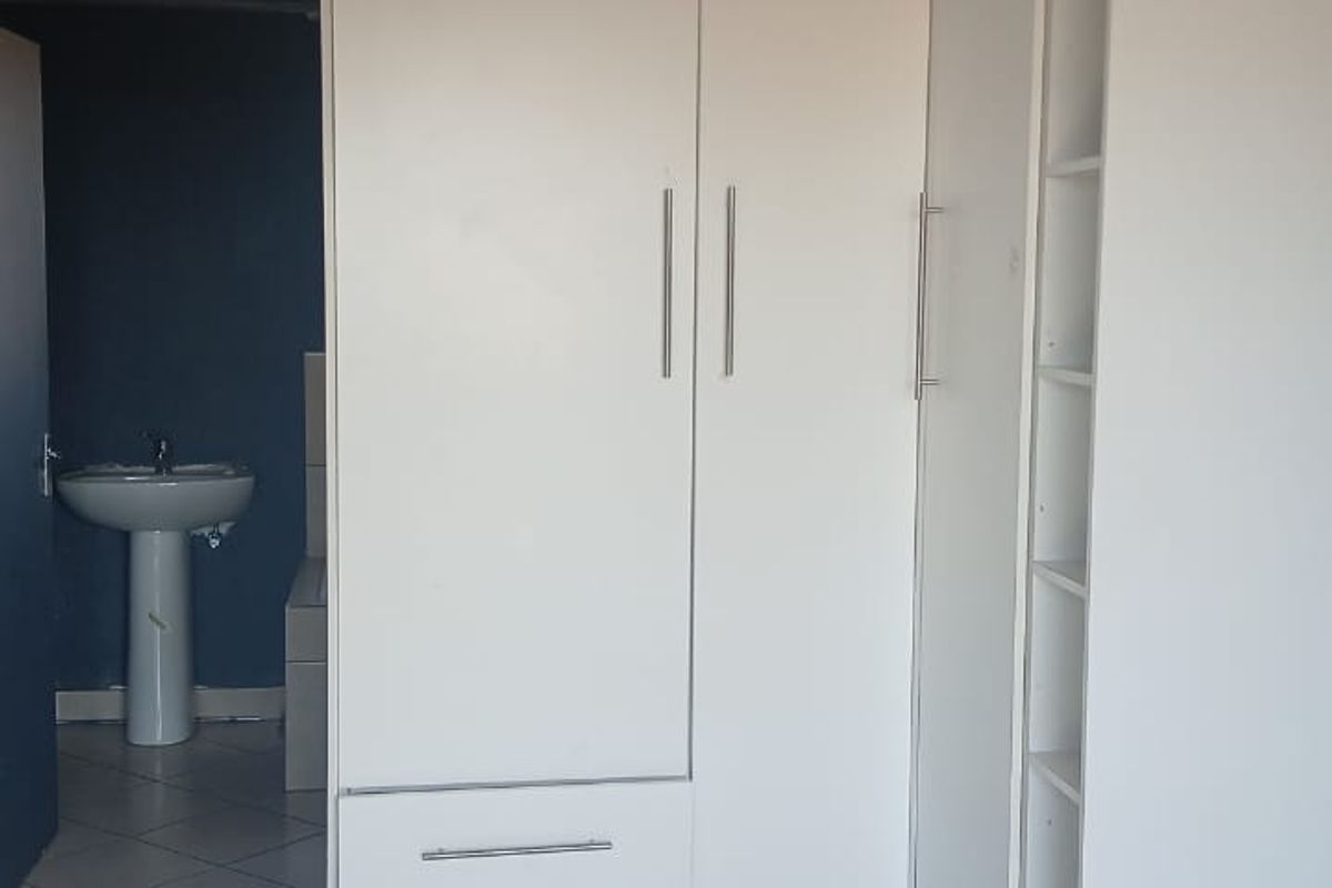 A bedroom featuring built-in white cabinetry and tiled flooring, with an adjacent view into a bathroom area with a pedestal basin.