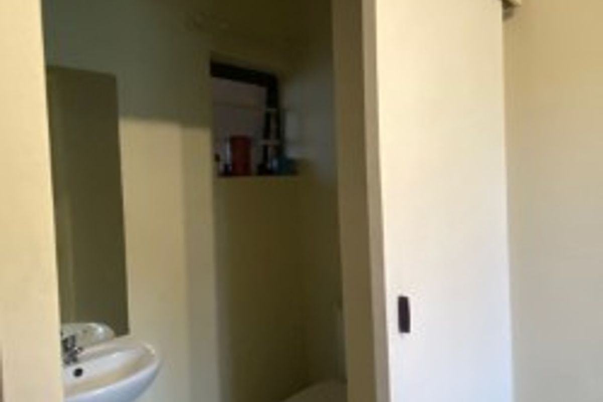 A functional bathroom featuring a pedestal basin, toilet, and a sliding door entry, finished with neutral wall tones and tiled flooring.