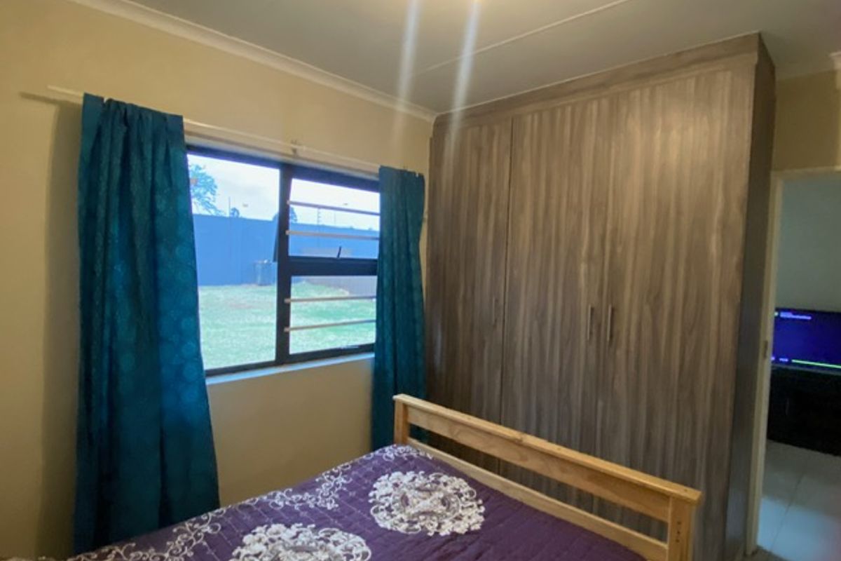 A bedroom featuring built-in wooden cupboards, an aluminium window with security bars, and neutral wall finishes.