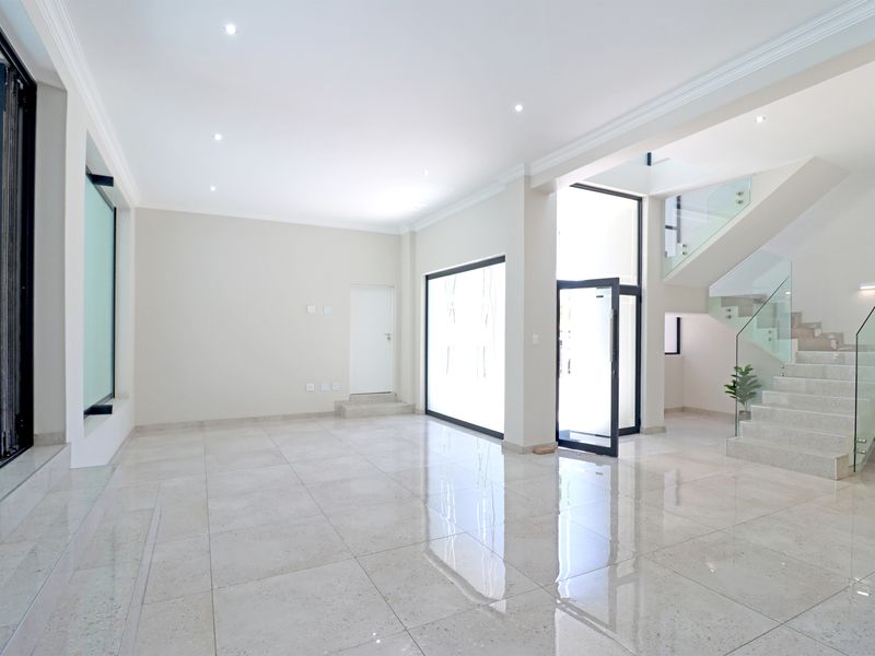 Spacious, modern open-plan living area featuring polished porcelain tiles, recessed lighting, and a contemporary staircase with a glass balustrade.