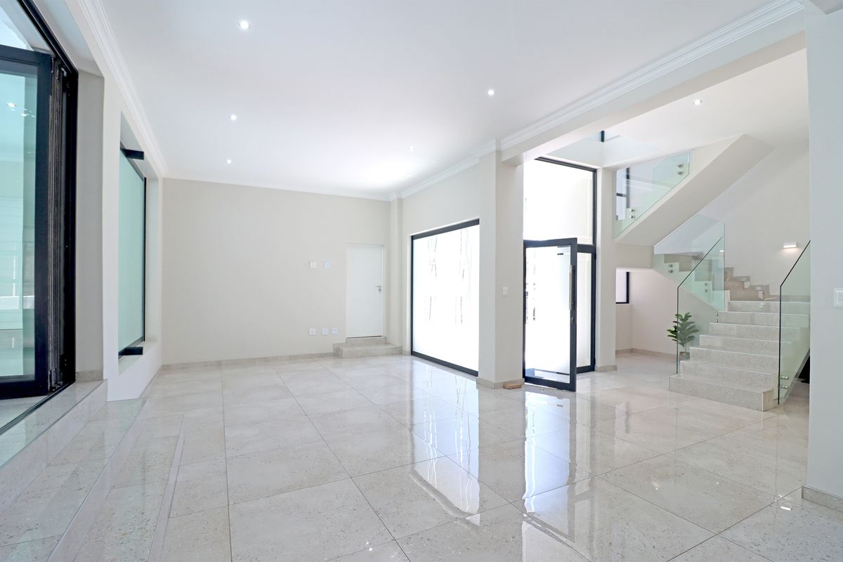 Spacious, modern open-plan living area featuring polished porcelain tiles, recessed lighting, and a contemporary staircase with a glass balustrade.