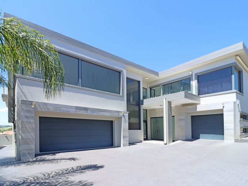Modern double-story residence featuring a paved driveway, double garage, and contemporary architectural design with stone cladding and glass balcony accents.