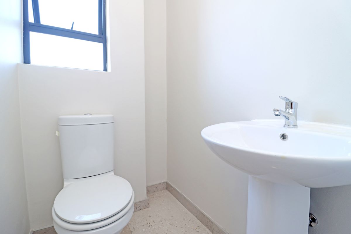 A clean and minimalist guest bathroom featuring a white pedestal basin and a standard toilet with neutral tiled flooring.