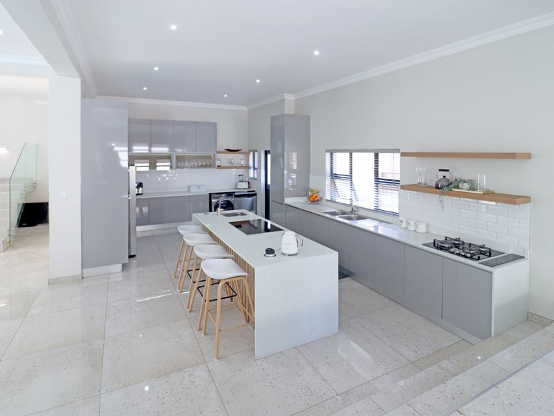 Modern open-plan kitchen featuring a central island with quartz countertops, built-in gas hob, sleek grey cabinetry, and high-quality porcelain floor tiles.