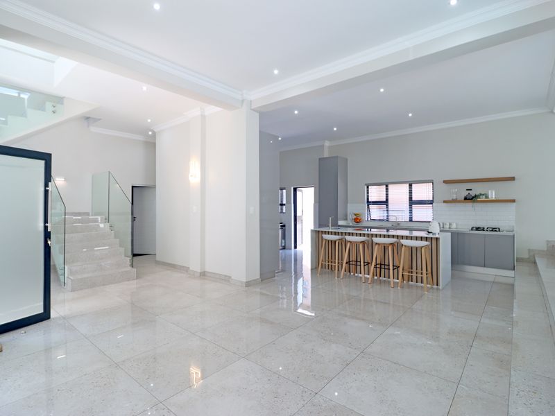 Spacious open-plan living area featuring a modern kitchen with a central island, sleek cabinetry, and a striking glass-railed staircase.