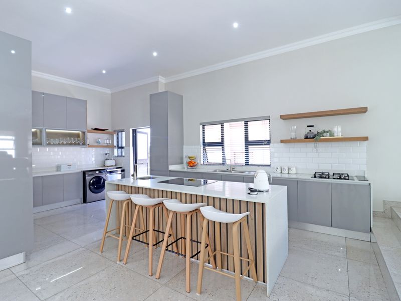 Modern, well-appointed kitchen featuring a central island with breakfast bar, sleek grey cabinetry, stone countertops, and high-quality integrated appliances.