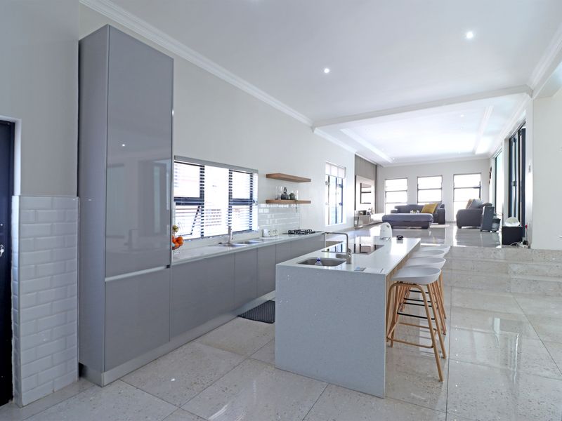 Modern open-plan kitchen featuring sleek grey cabinetry, a central island with quartz countertops, and seamless transition to the elevated living area.