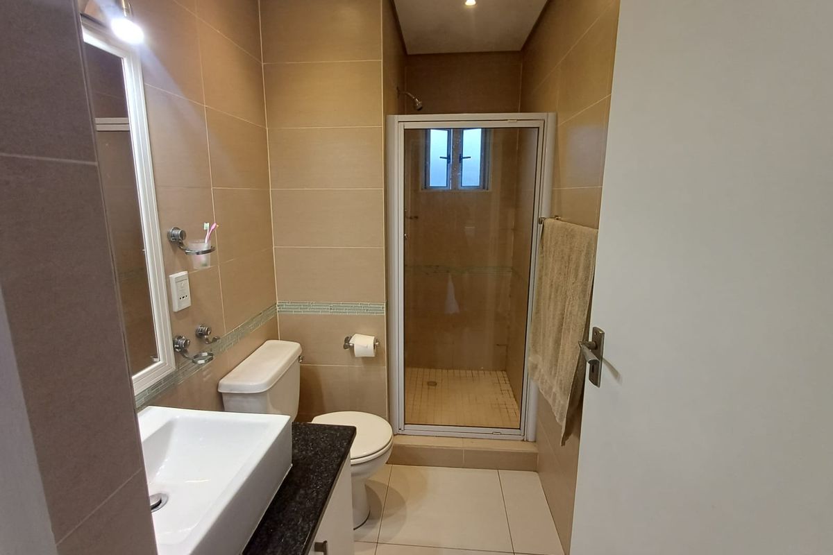 A functional bathroom featuring a shower enclosure, vanity basin with granite countertop, and neutral tiled finishes throughout.
