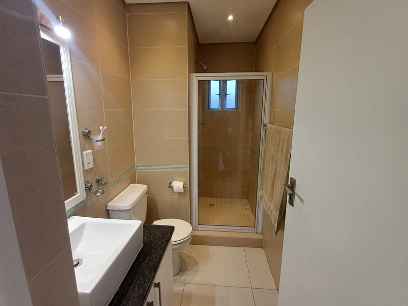 A functional bathroom featuring a shower enclosure, vanity basin with granite countertop, and neutral tiled finishes throughout.