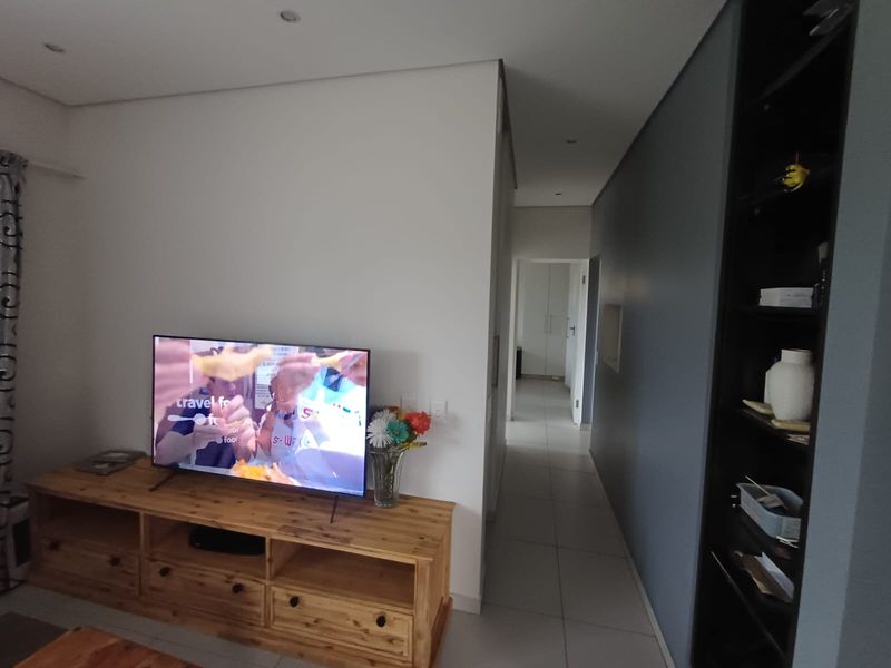 A living area featuring tiled flooring, recessed downlighting, and a built-in shelving unit, leading into a hallway.