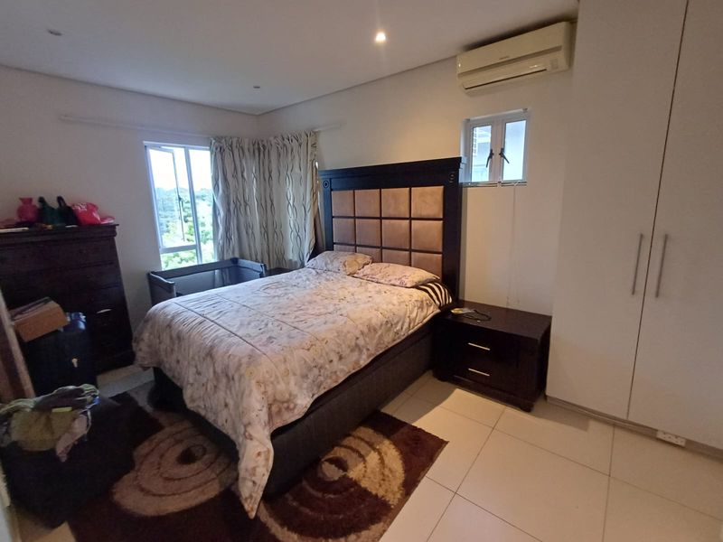 A functional bedroom featuring tiled flooring, built-in cupboards, and a wall-mounted air conditioning unit, offering a comfortable and practical living space.