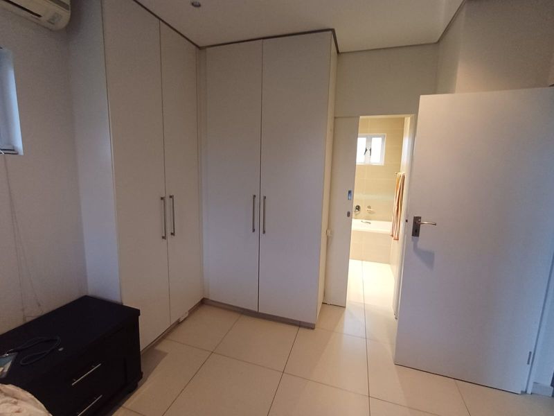 A bedroom featuring built-in cupboards, tiled flooring, and an air conditioning unit, with an adjoining bathroom visible through the doorway.