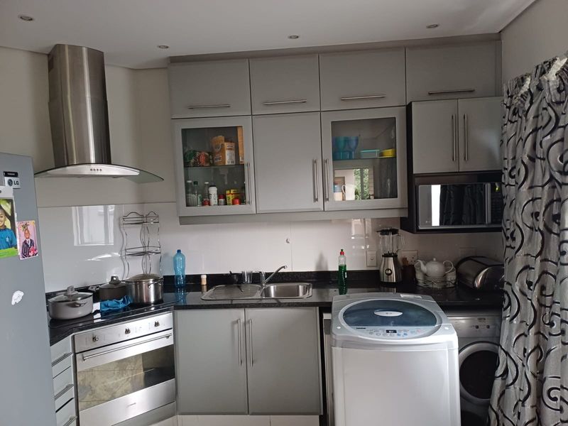 A functional kitchen featuring modern grey cabinetry, granite countertops, integrated stainless steel appliances, and a built-in oven with an extractor fan.