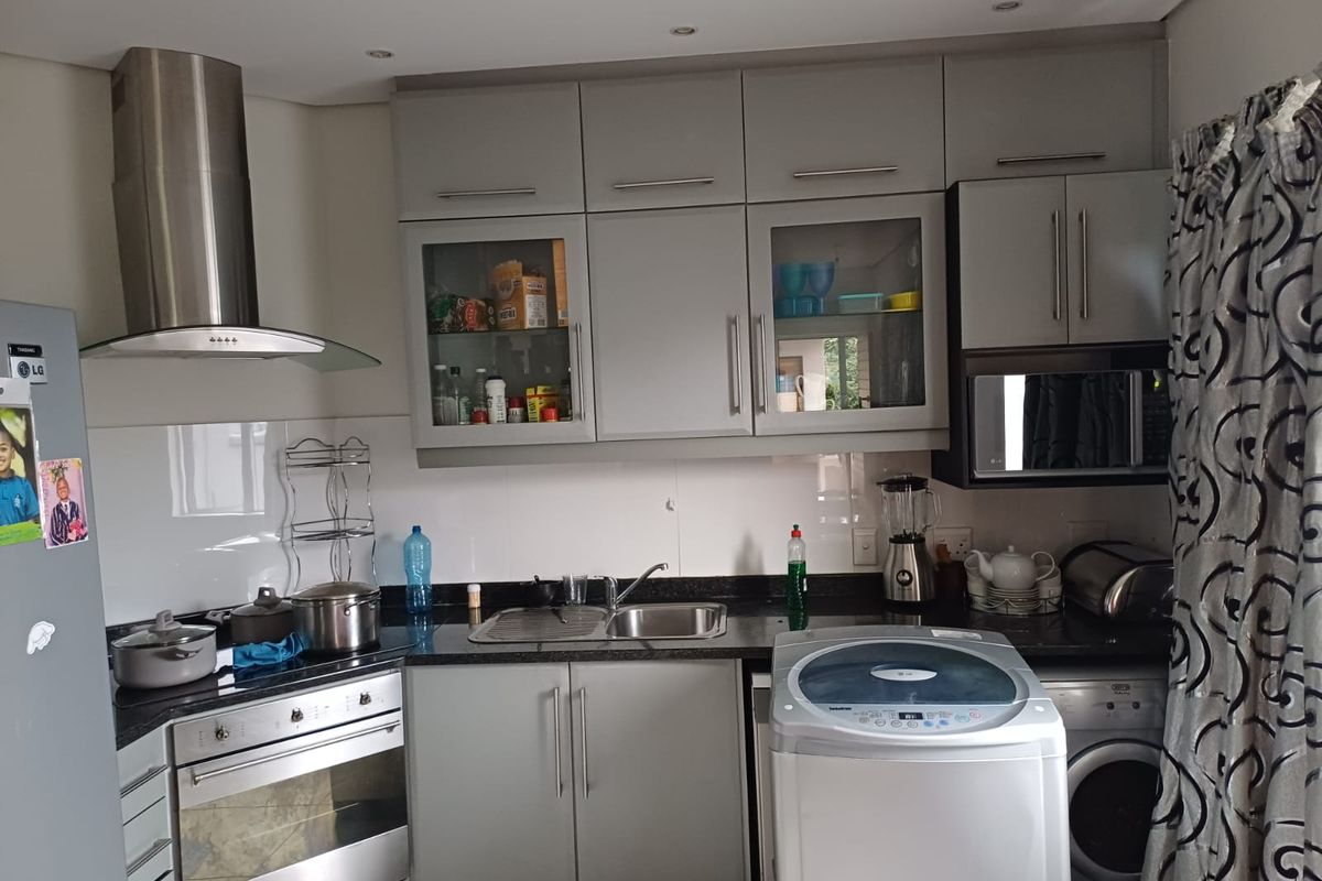 A functional kitchen featuring modern grey cabinetry, granite countertops, integrated stainless steel appliances, and a built-in oven with an extractor fan.