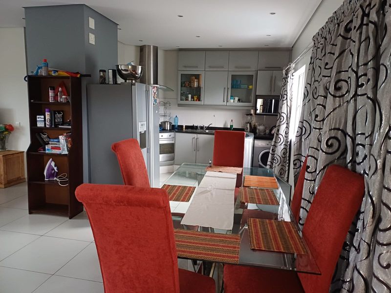 Open-plan kitchen and dining area featuring modern grey cabinetry, built-in appliances, and tiled flooring, creating a functional and connected living space.