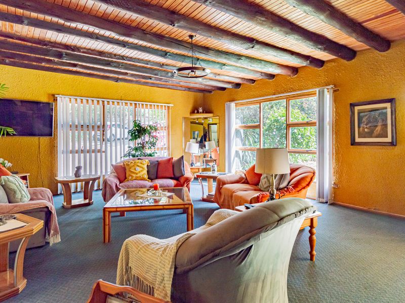 Spacious living room featuring a rustic exposed timber beam ceiling, textured walls, and large windows providing ample natural light.