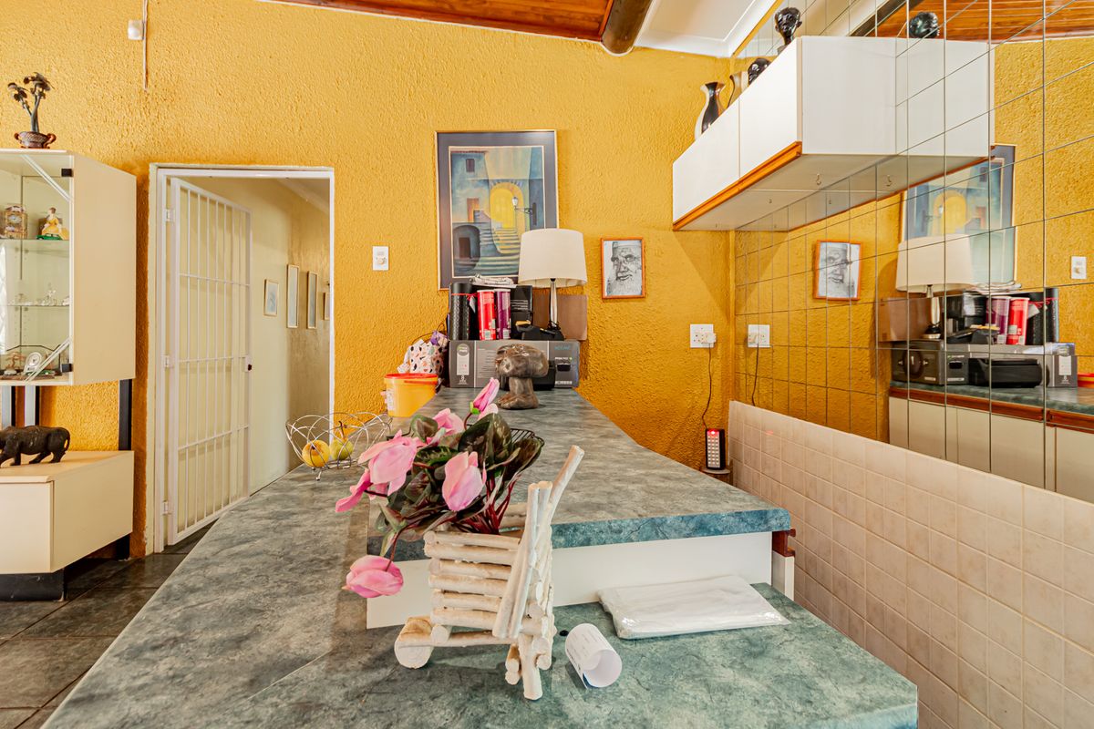 A dated kitchen area featuring a built-in breakfast bar, mirrored wall accents, and exposed timber ceiling beams, offering potential for modern renovation.