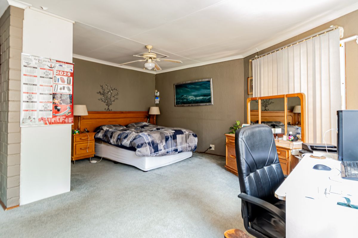 Spacious bedroom featuring carpeted flooring, a ceiling fan, and vertical blinds, offering a functional layout with ample space for bedroom and office furniture.