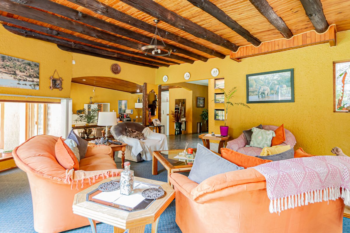 Spacious living room featuring a rustic exposed timber beam ceiling, textured yellow walls, and a decorative stained glass window.
