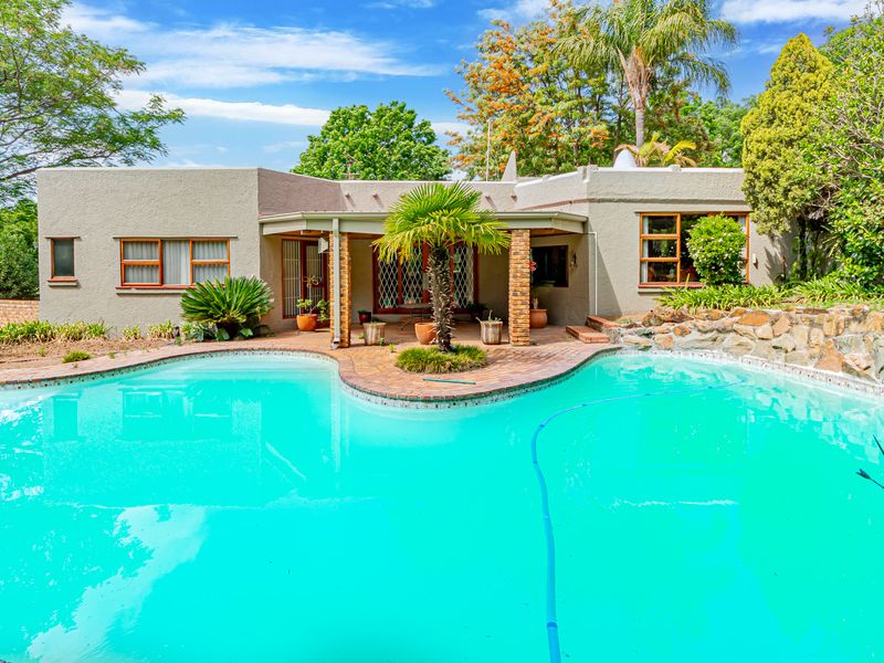 A well-maintained swimming pool area featuring a stone retaining wall, brick-paved surround, and a covered patio area with brick pillars.