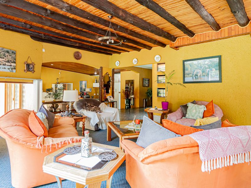 Spacious living room featuring a rustic exposed timber beam ceiling, textured yellow walls, and a decorative stained glass window.