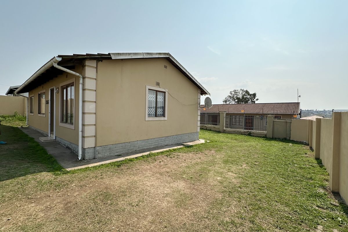 Side view of the house showing the exterior facade, security window bars, and surrounding garden area with perimeter walling.