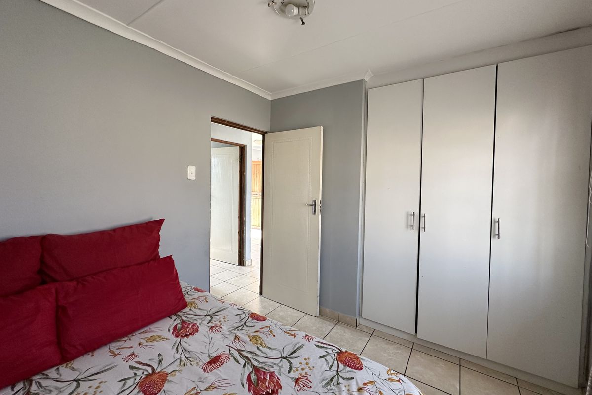 A bedroom featuring built-in white cabinetry, tiled flooring, and neutral grey walls, providing a functional and clean living space.