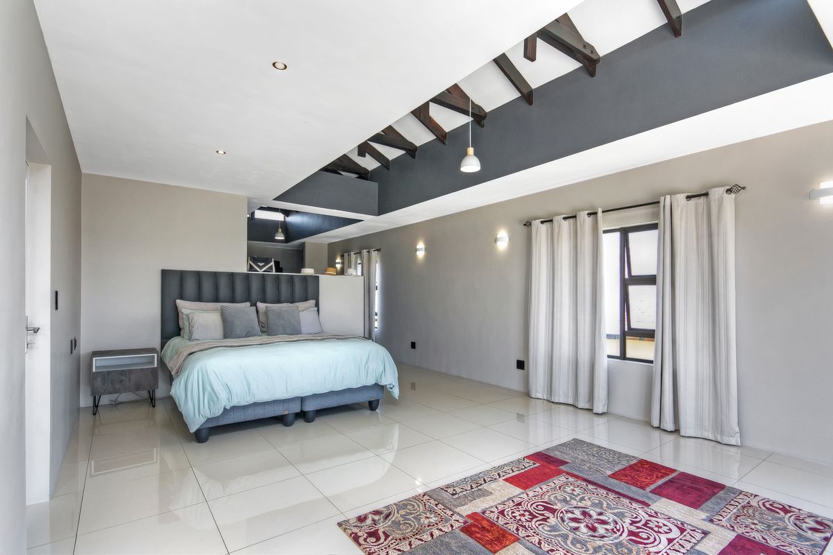 Spacious bedroom featuring high ceilings with exposed timber beams, polished porcelain floor tiles, and large windows with integrated curtain tracks.