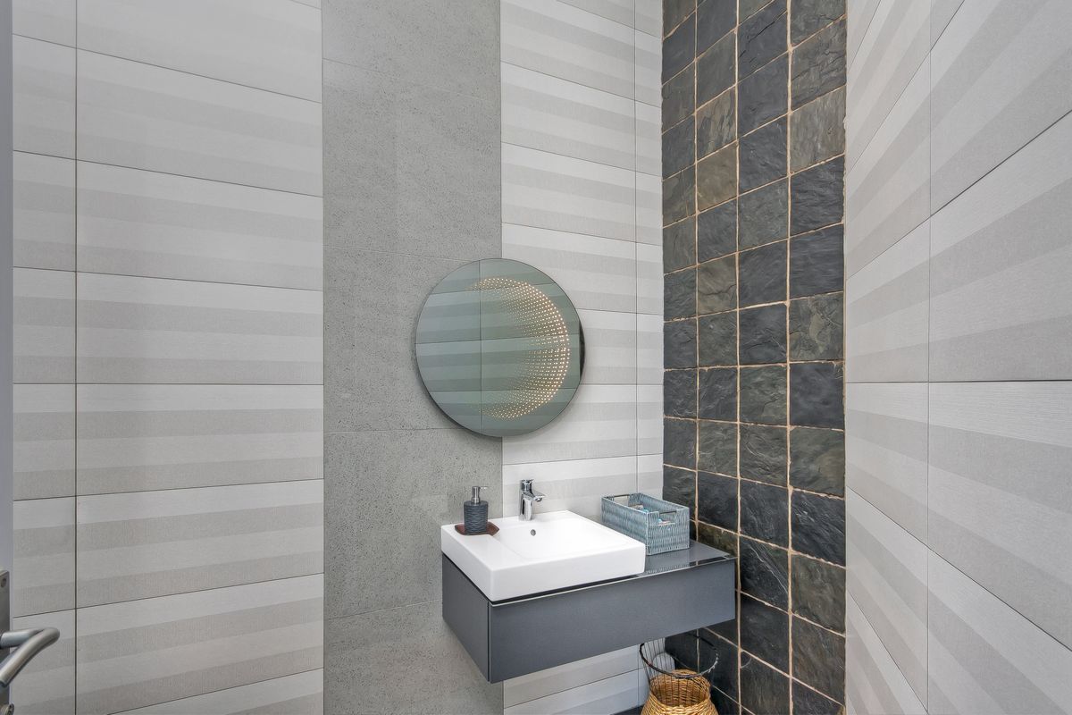 Modern guest bathroom featuring a wall-mounted vanity with a sleek basin, contemporary tiled walls, and a decorative illuminated circular mirror.