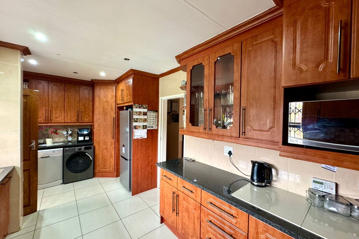 A functional kitchen featuring traditional wood cabinetry, granite countertops, tiled flooring, and integrated space for laundry appliances.