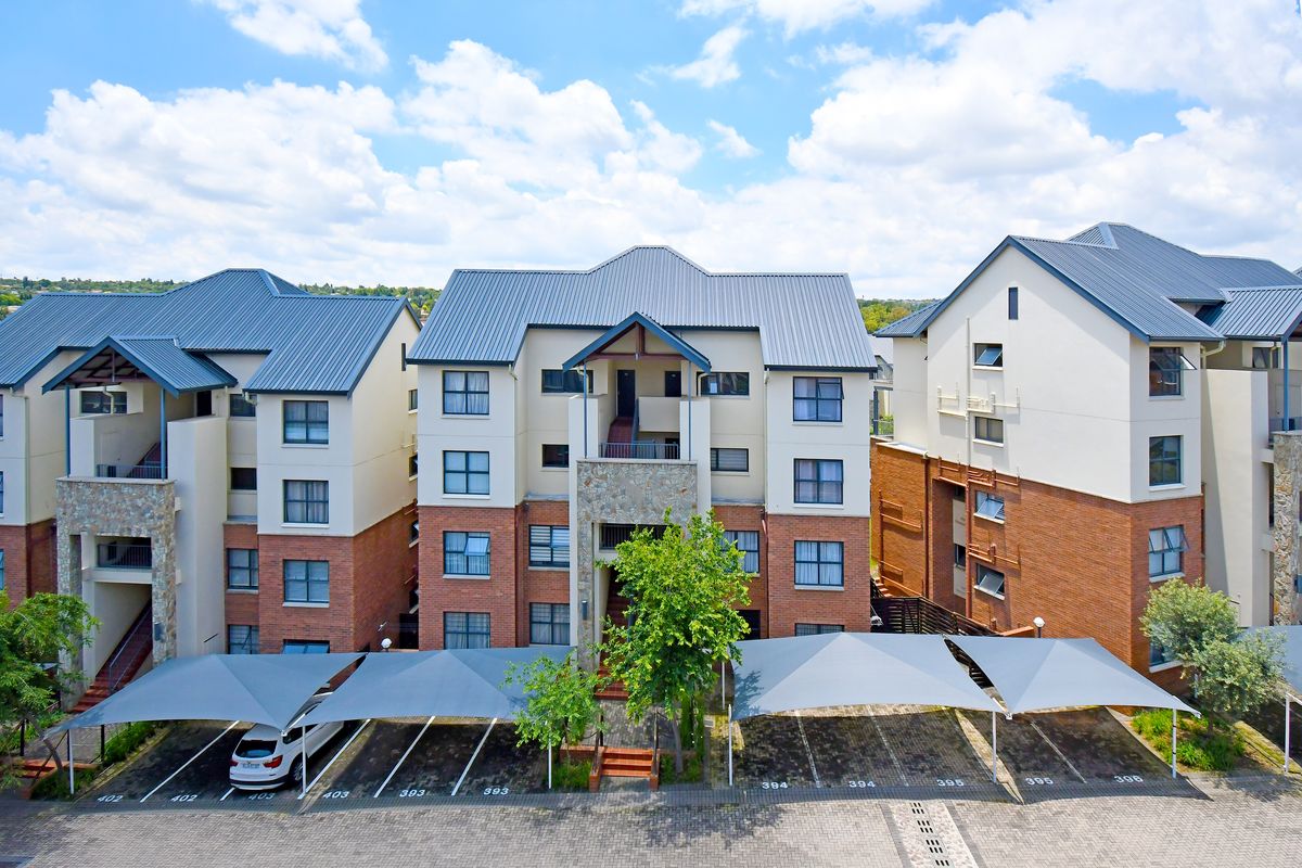 Aerial view of a multi-story apartment complex featuring brick and plaster facades, pitched metal roofing, and designated covered parking bays.