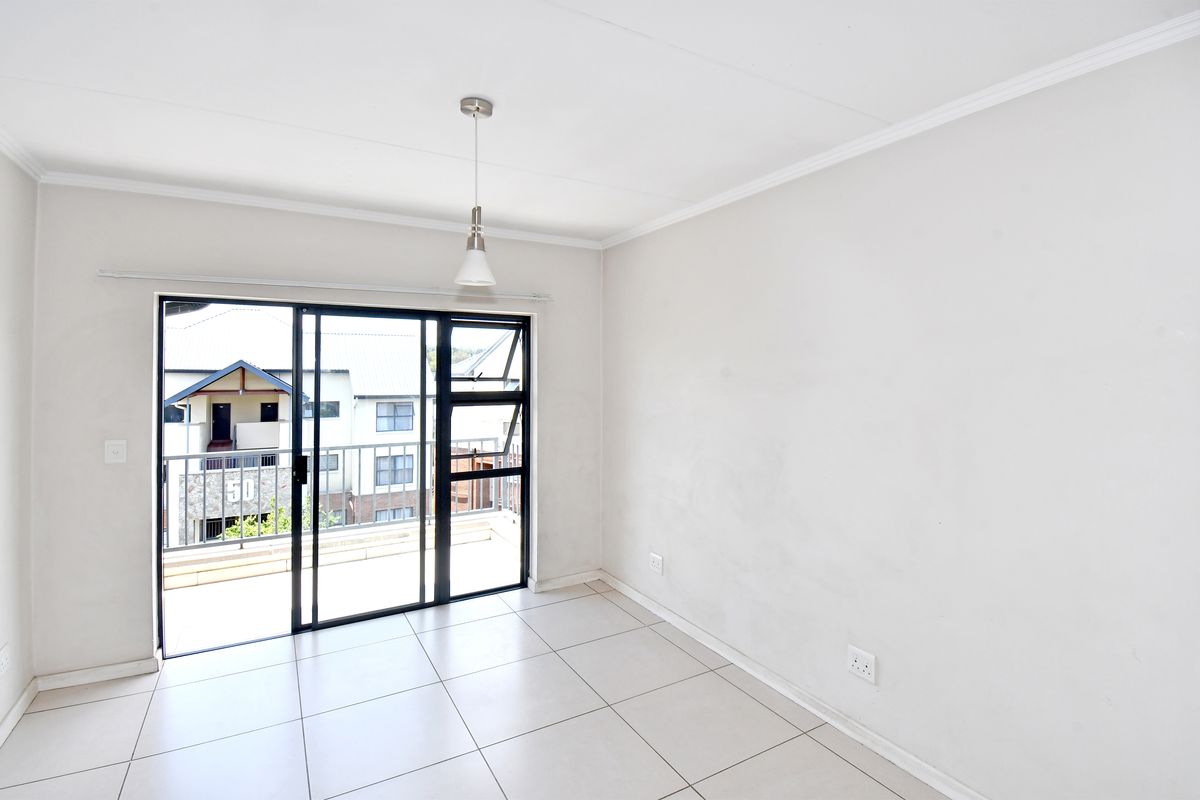 A bright, empty living area featuring neutral floor tiles, a modern pendant light, and large sliding glass doors leading to a private balcony.