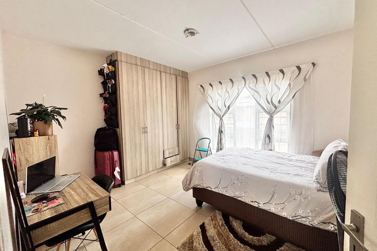 A well-lit bedroom featuring built-in wooden cabinetry, tiled flooring, and large windows allowing for natural light.
