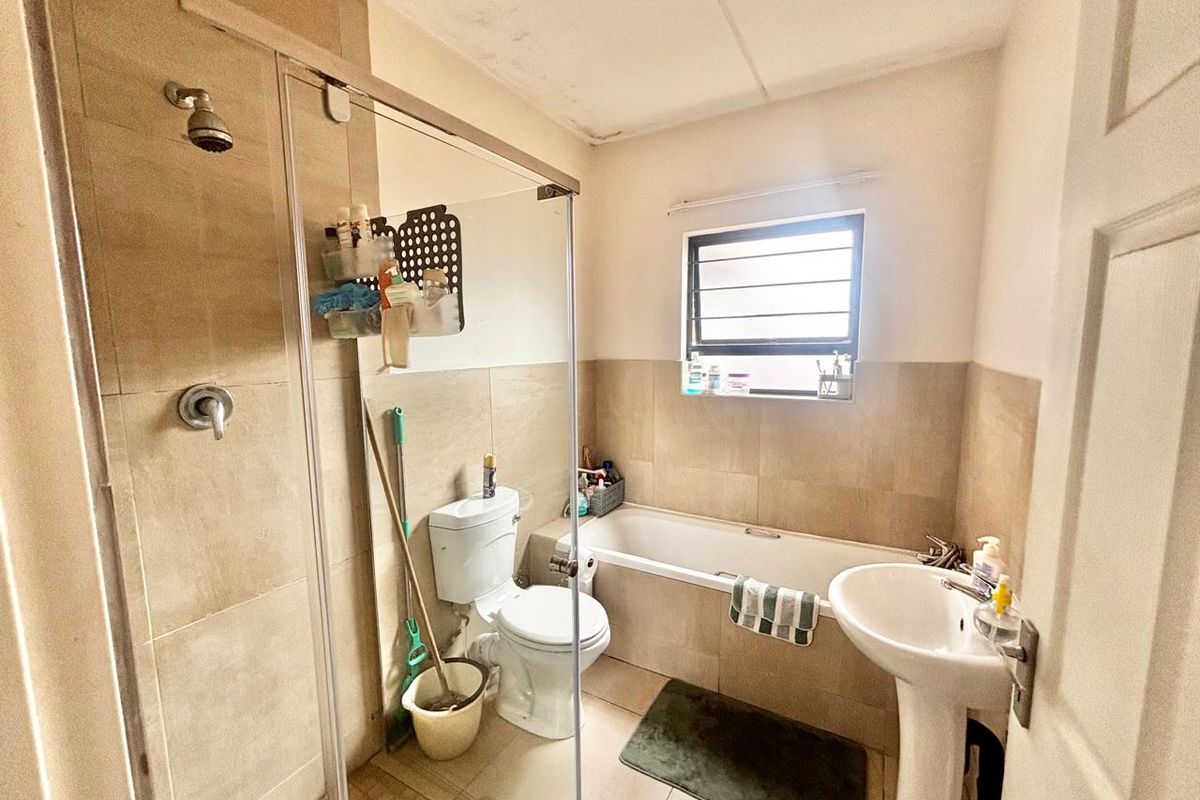 A functional bathroom featuring a glass-enclosed shower, a bathtub, a pedestal sink, and a toilet with neutral wall tiling.