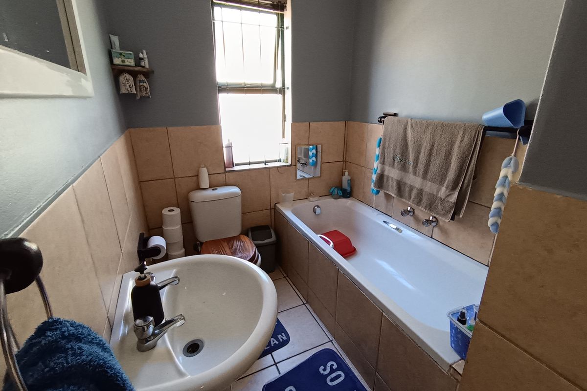 A functional bathroom featuring a built-in bathtub, pedestal basin, and toilet with tiled splashbacks and a window for natural light.