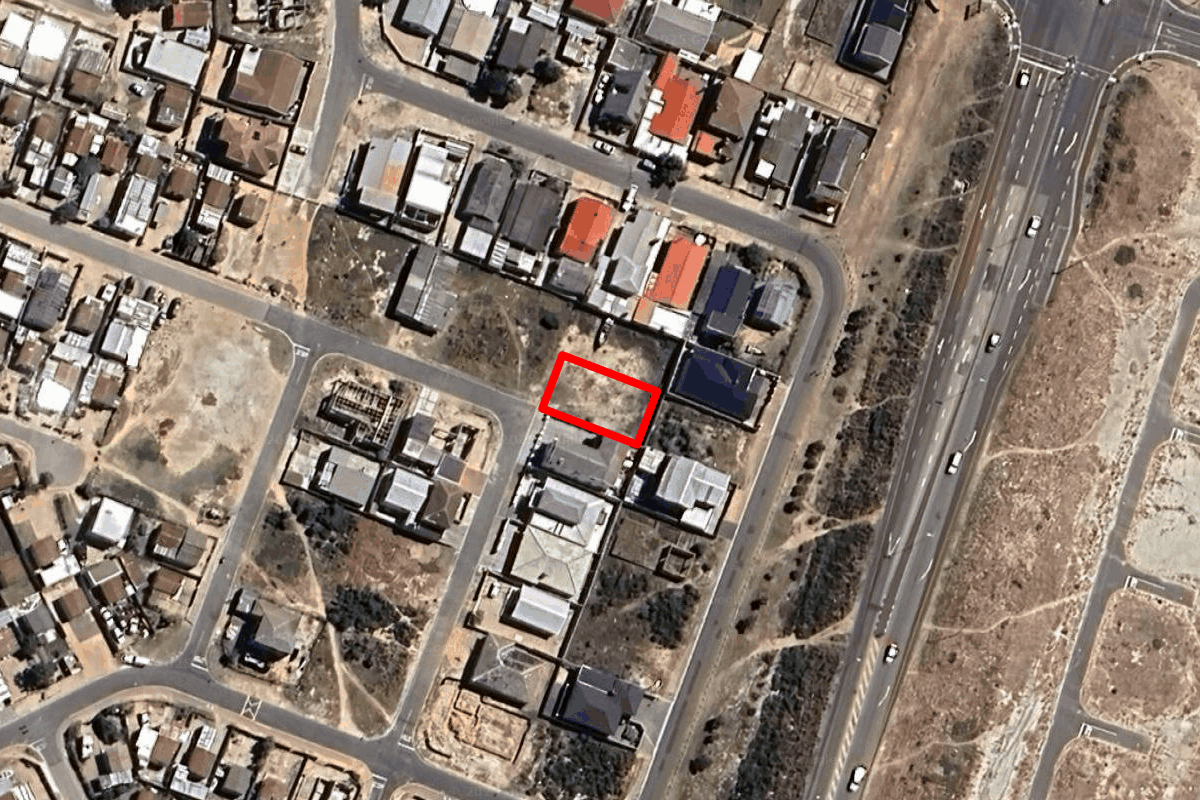 An aerial view showing a vacant residential plot highlighted in red within an established suburban neighborhood.