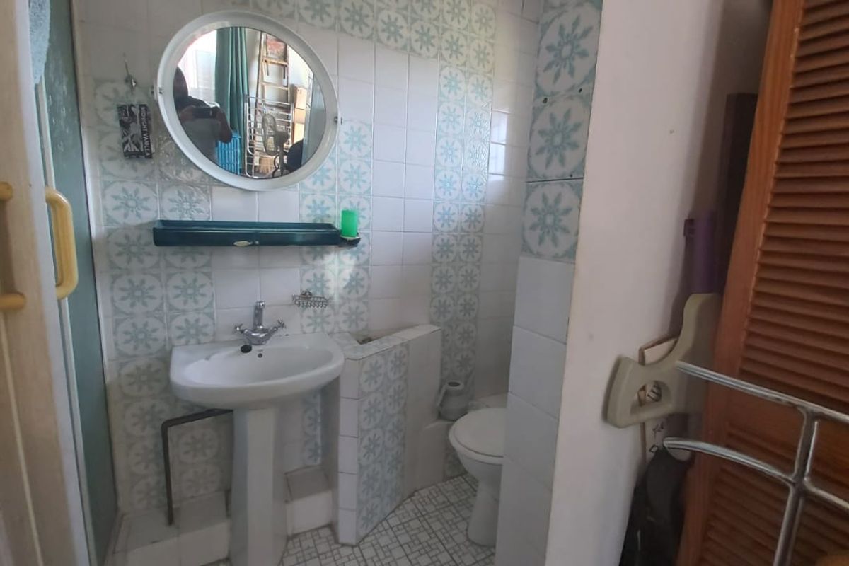 A compact bathroom featuring a pedestal sink, toilet, and dated decorative wall tiling with a louvered door entrance.