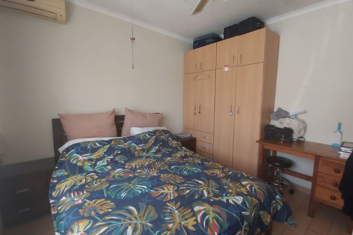 A functional bedroom featuring a built-in wardrobe, ceiling fan, and wall-mounted air conditioning unit.