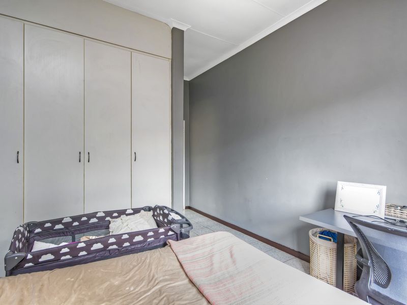 A bedroom featuring built-in cupboards, tiled flooring, and a neutral grey accent wall, providing a functional space with ample storage.