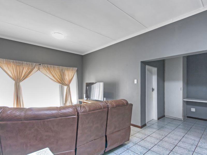 A living room featuring tiled flooring, neutral grey walls, and a built-in cupboard, offering a functional and well-maintained living space.