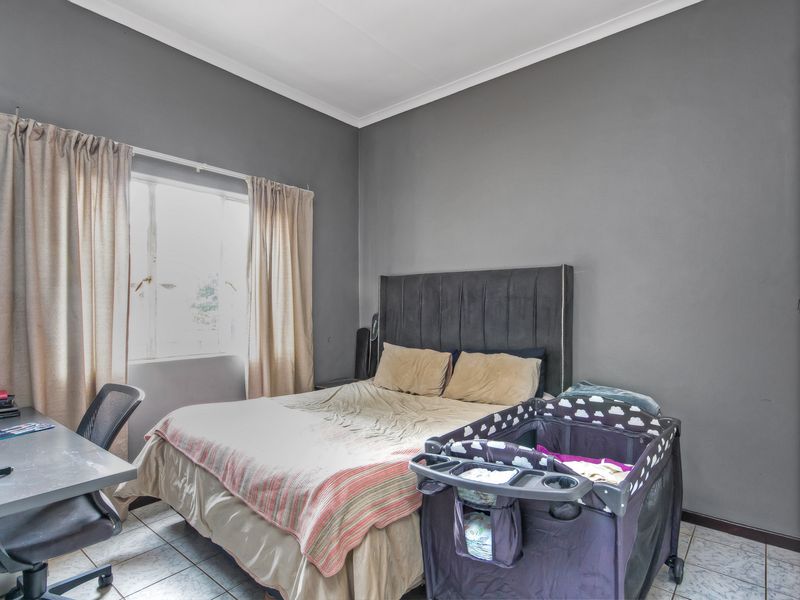 A bedroom featuring tiled flooring, coved ceilings, and a built-in wardrobe, providing a functional space with neutral grey wall finishes.