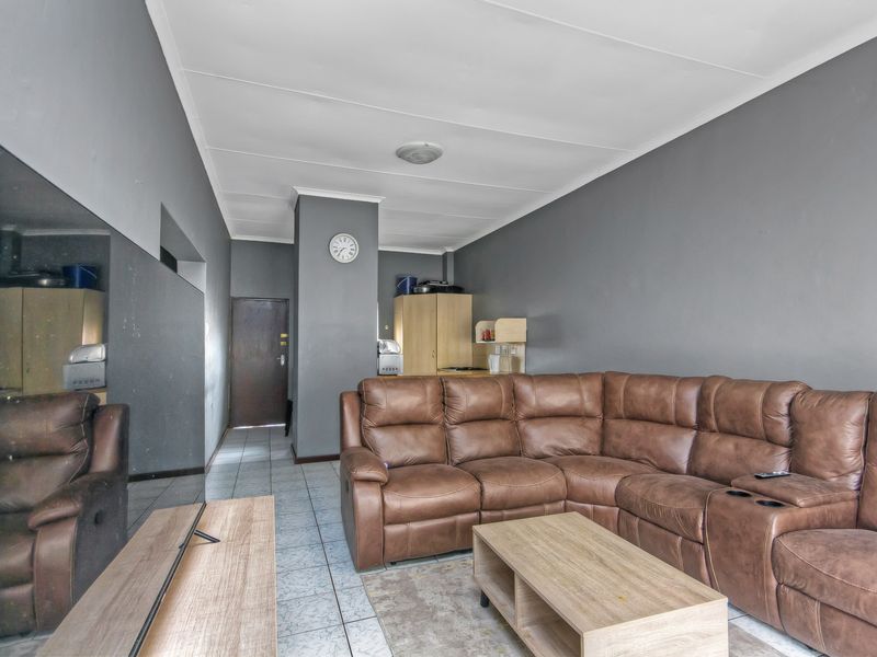 A living room area featuring tiled flooring and grey painted walls, providing a functional space with direct access to the apartment entrance.