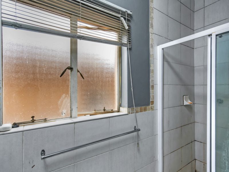 A bathroom featuring a shower enclosure, tiled walls, and a frosted glass window with a venetian blind.