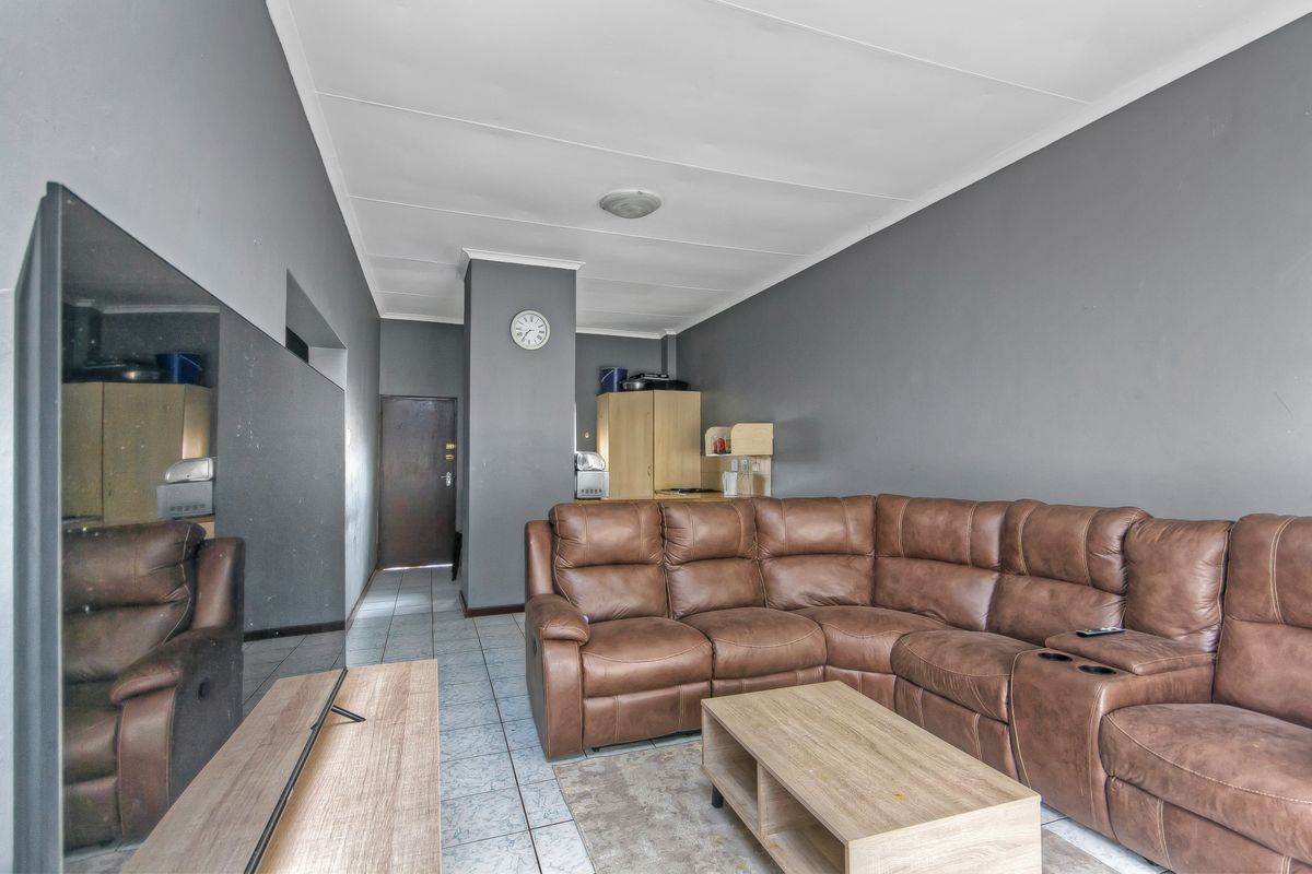 A living room area featuring tiled flooring and grey painted walls, providing a functional space with direct access to the apartment entrance.