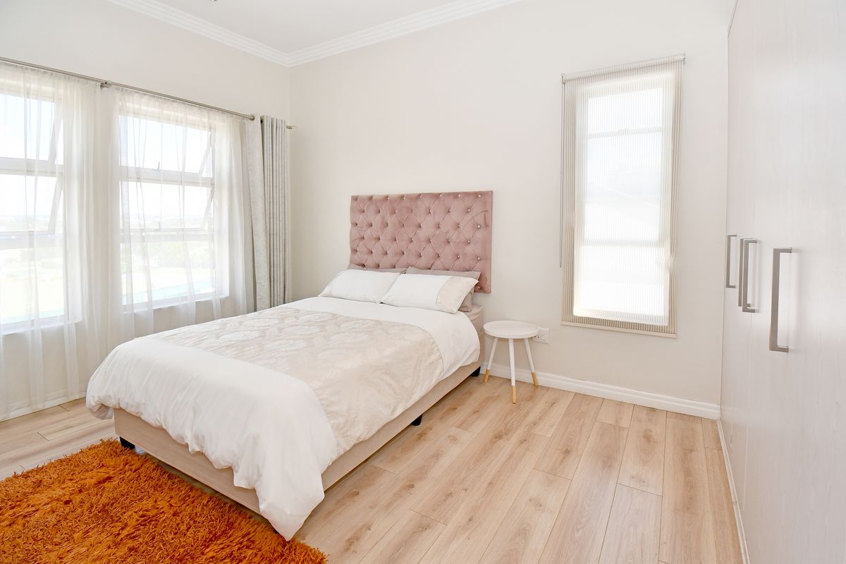 A bright and well-maintained bedroom featuring light wood-look flooring, built-in wardrobes, and large windows that provide ample natural light.