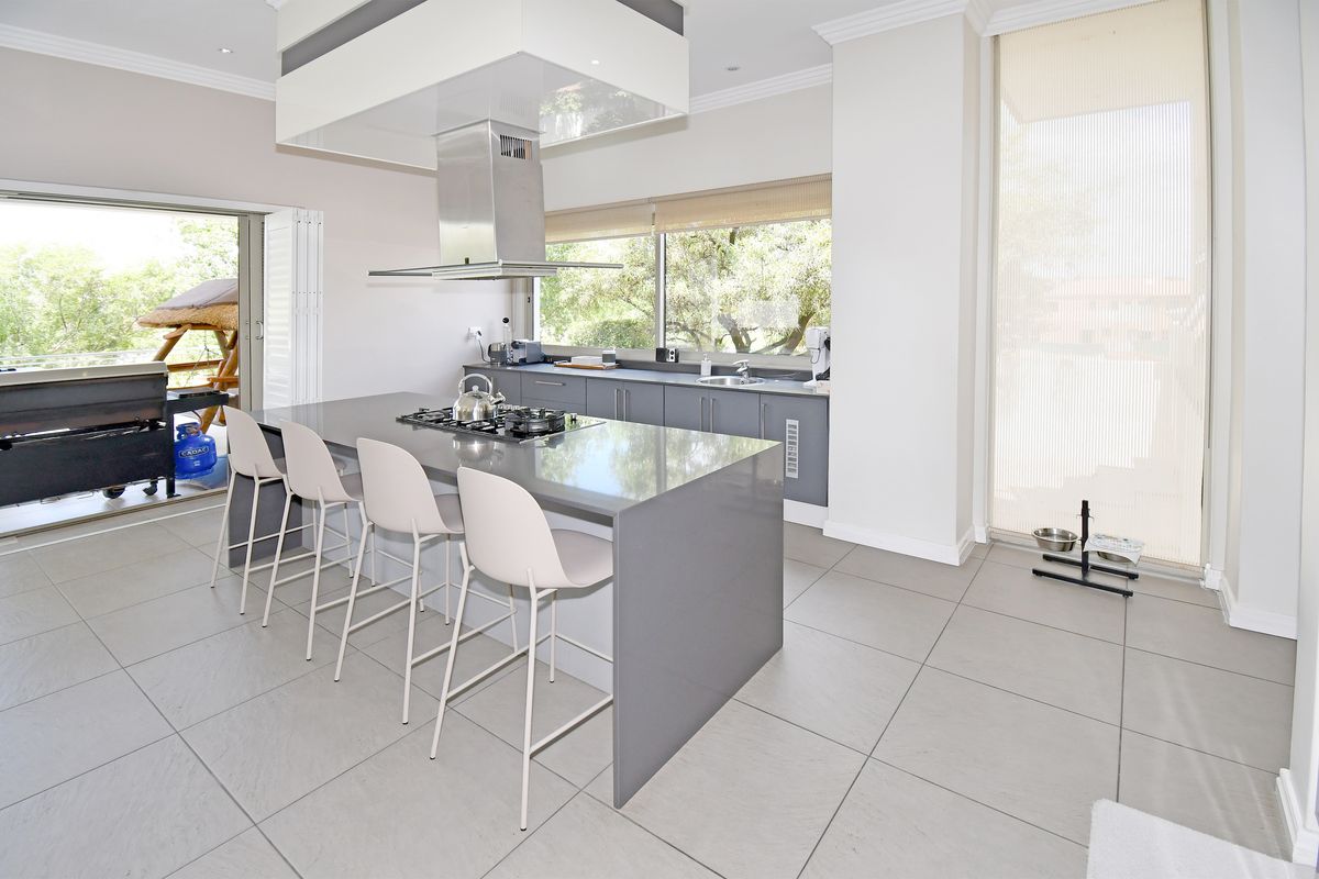 Modern kitchen featuring a large central island with integrated gas cooktop, stainless steel extractor hood, and sleek grey cabinetry with stone countertops.