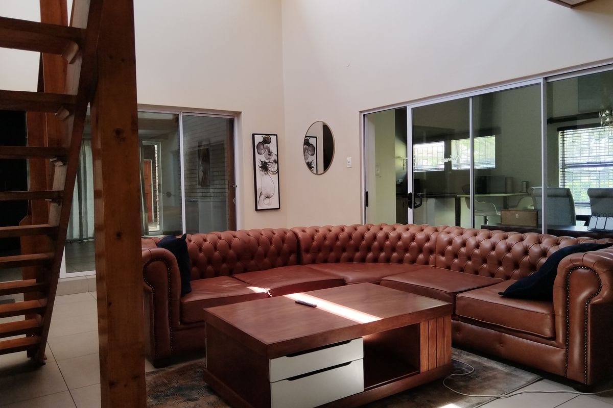 Spacious double-volume living room featuring tiled flooring, a wooden staircase, and large sliding glass doors providing natural light and garden access.