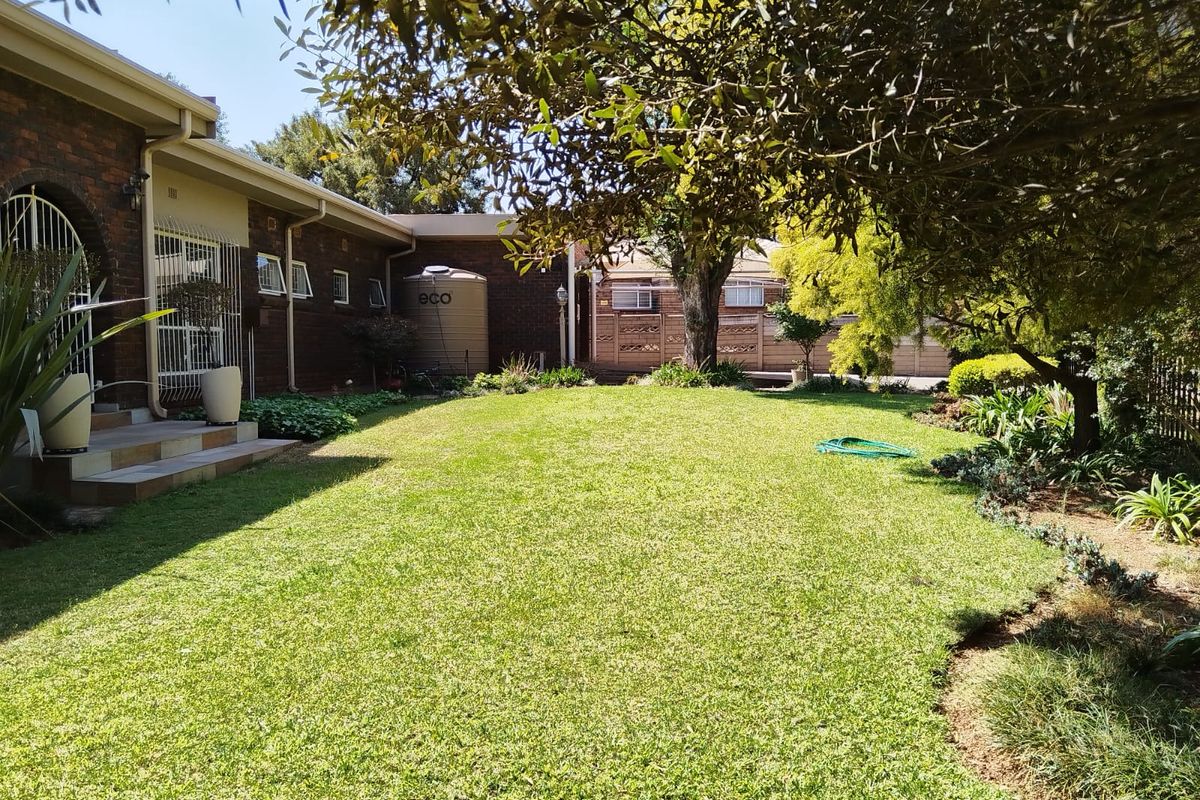 A well-maintained rear garden featuring a lush lawn, mature trees, brick exterior walls, and a functional water tank.